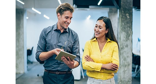 Two employees walking down a hall looking at an iPad