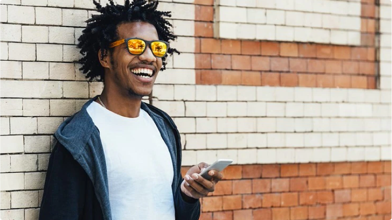 Man leaning against a brick wall, while looking at his cellphone.