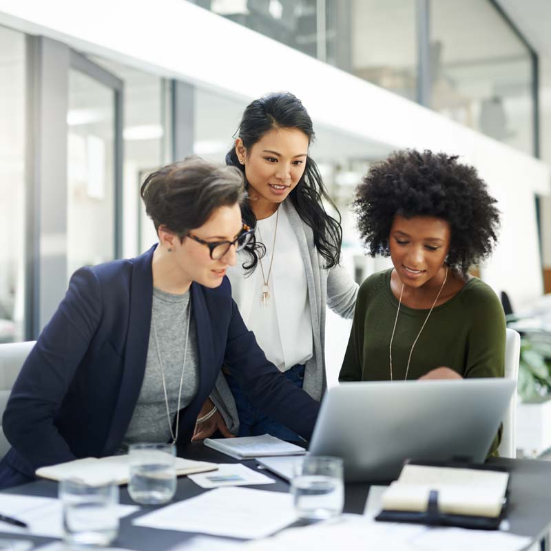 Three women gathered around a laptop looking at it