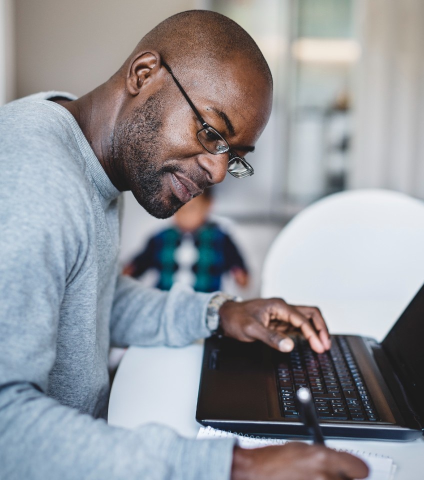 Man at his laptop writing on a note pad
