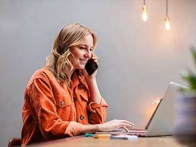 Woman at her laptop while talking on her phone 