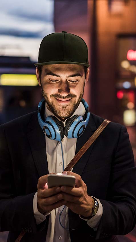Man with blue headphones around his neck looking at his phone at night