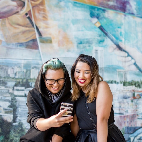 Two young people in front of a mural looking at a phone and smiling