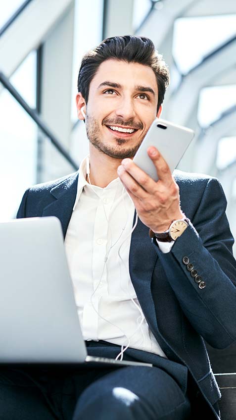 Man in suit with laptop on lap and headphones talking on phone