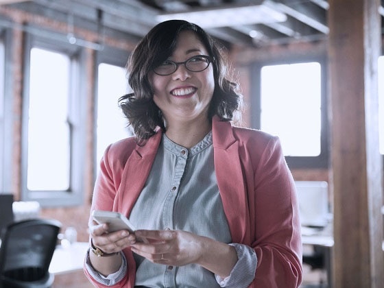 Asian woman with glasses smiling as she holds her phone
