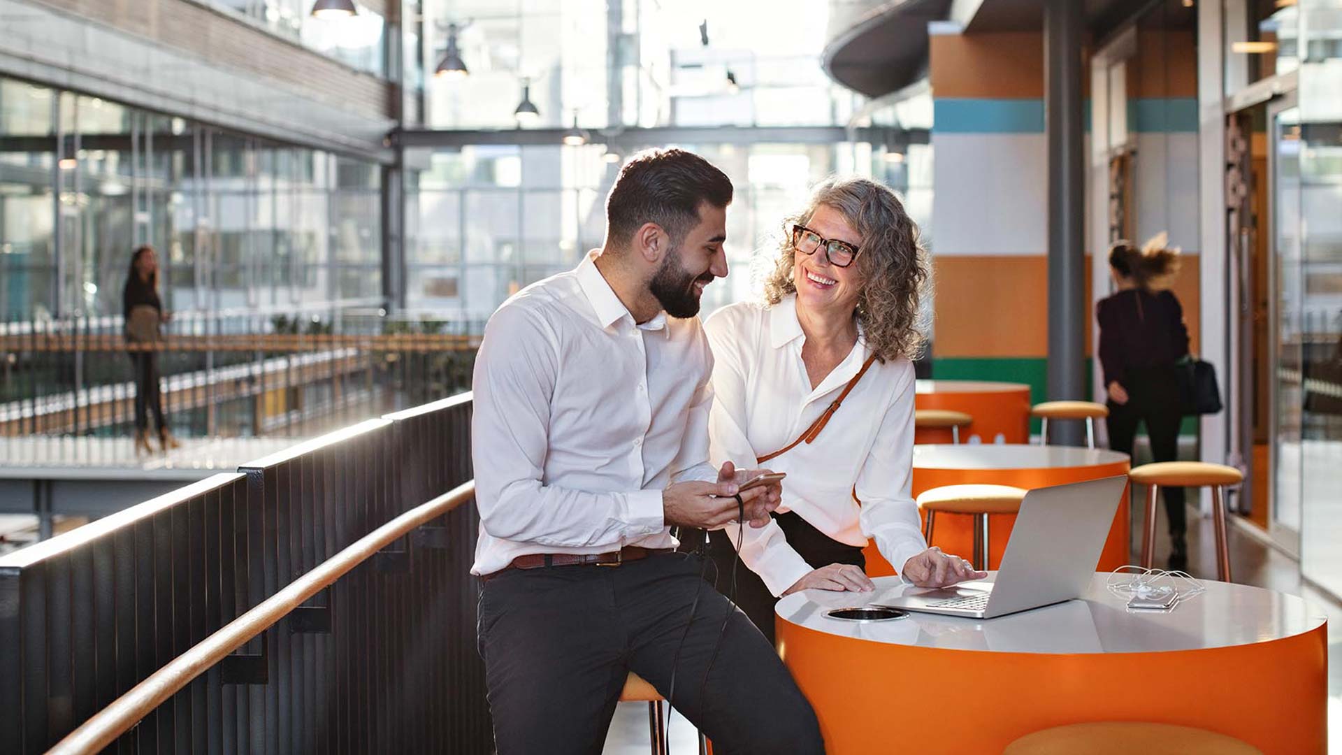 Two coworkers outside of office using phone and laptop.
