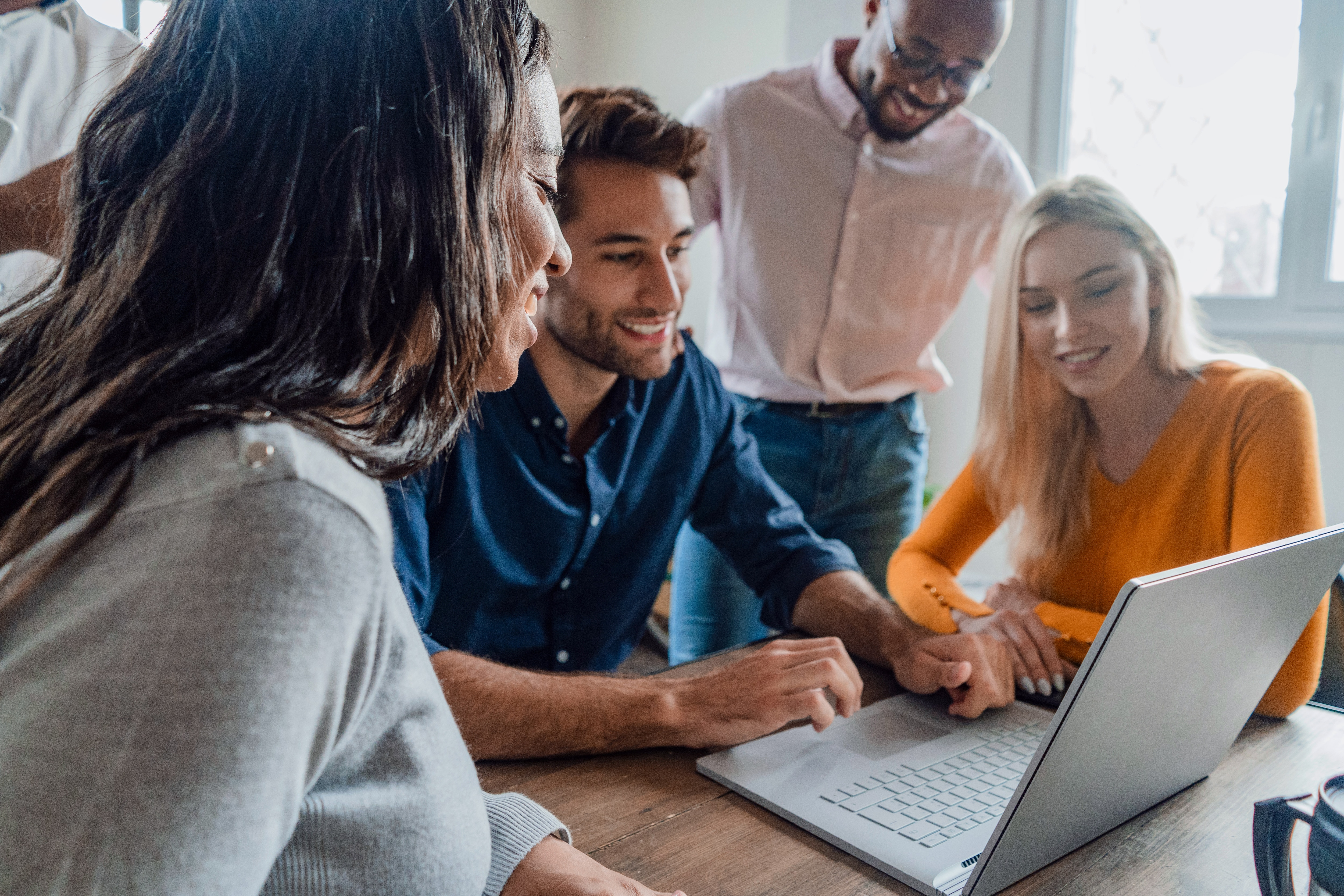 Group of people gathered around a laptop smiling and looking at the screen