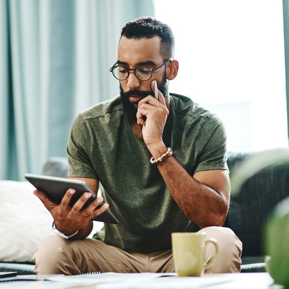 Man in green shirt and black glasses holding a pen and looking at his tablet