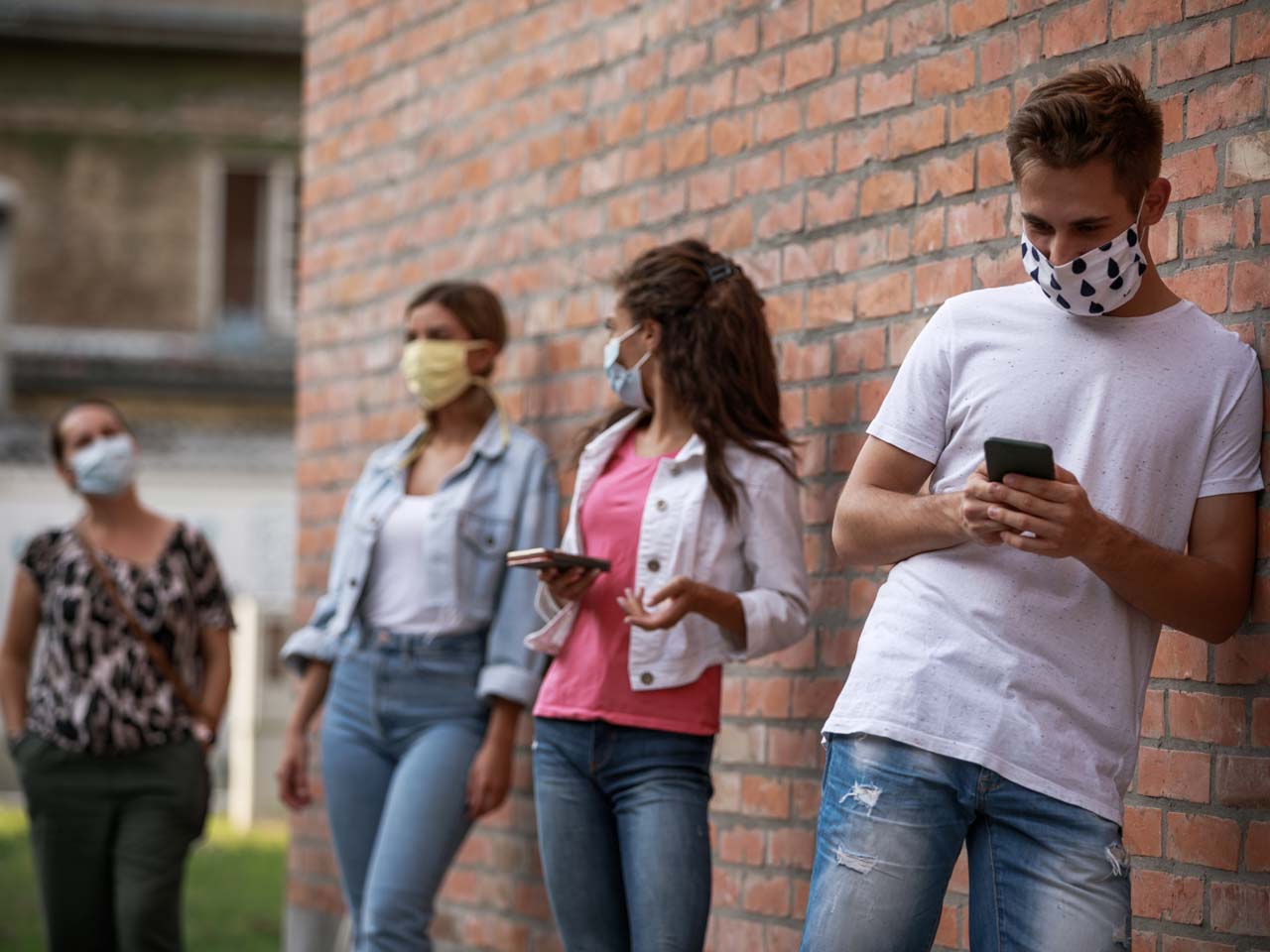 people socially distanced leaning against a brick wall