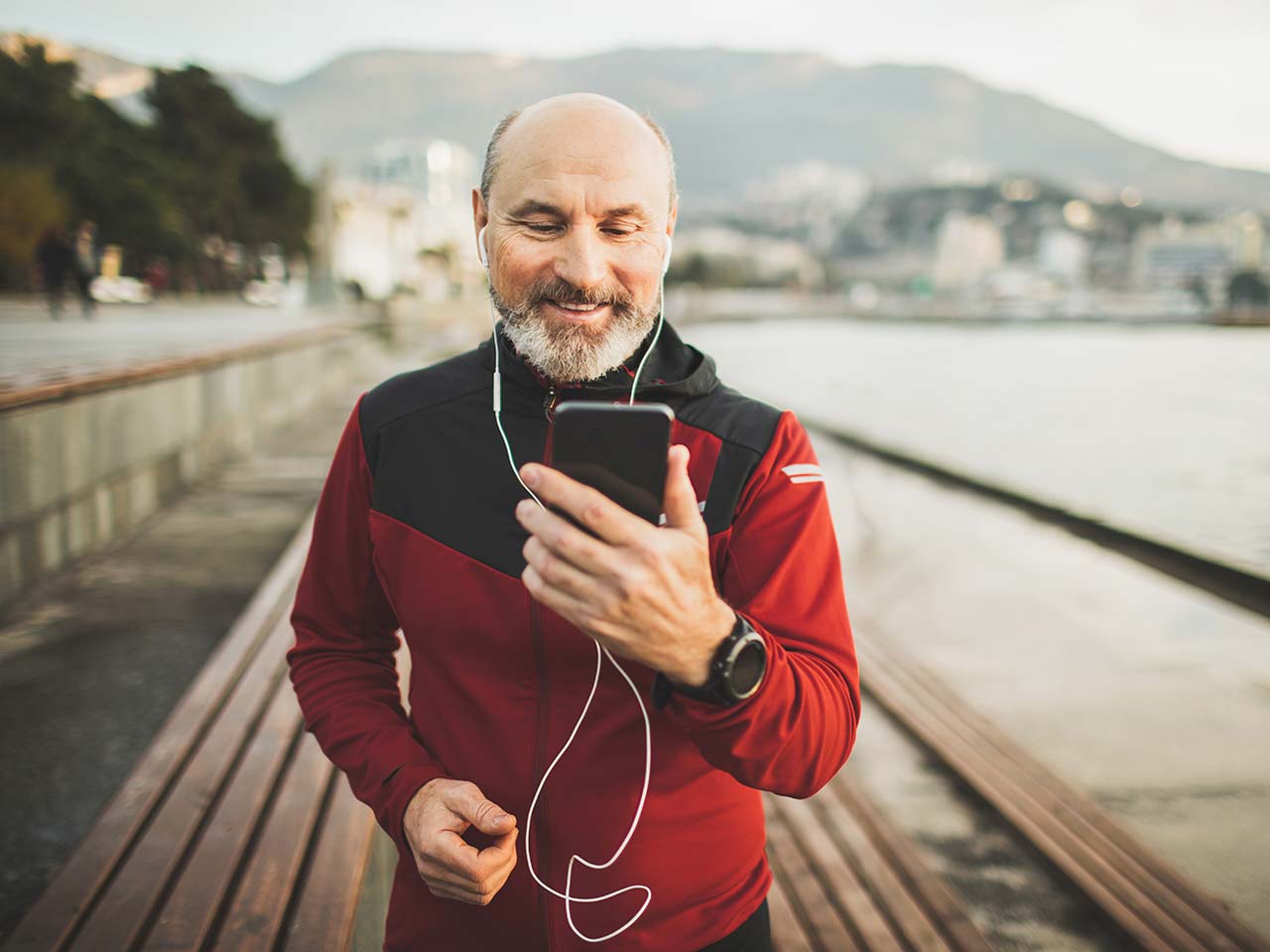 Older man out on a jog with headphones on looking at his mobile phone and smiling