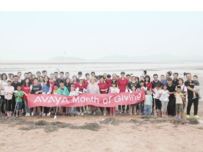 Avaya employees and their families posing on a beach with month of giving sign